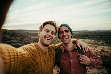 Caucasian male friends hiking in wilderness taking selfie with cellular device embracing the...