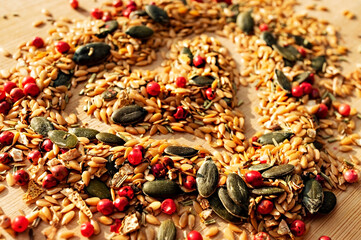 Food background of mix of spices, condiments and seeds close up with selective focus in shape of heart on wooden board, golden flax seeds, pumpkin seeds, red peppers, dried healthy food, mixture