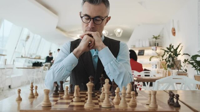 A close-up cropped view of a handsome man is playing chess sitting inside