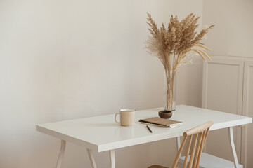 Aesthetic minimal office workspace interior design. Mug, notebook, pampas grass floral bouquet on...