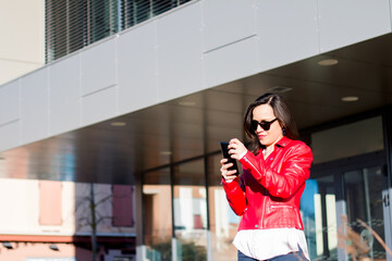 Happy and elegant woman in red wearing a smartphone standing on the street