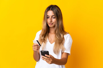 Fototapeta premium Young hispanic woman over isolated yellow background buying with the mobile with a credit card