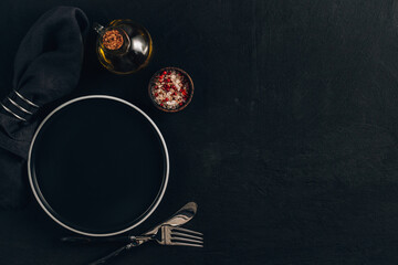 Elegant black table setting: plate, napkin and silverware over black background.