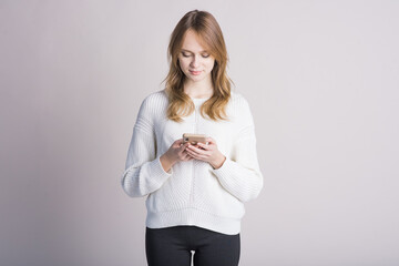 Portrait of a beautiful girl on a white background in the studio who uses a smartphone