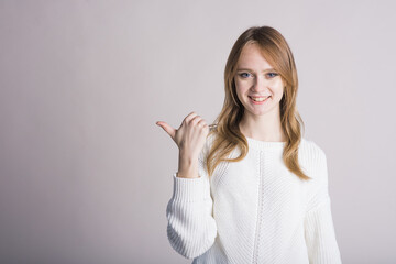 Portrait of a stylish girl on a white background in the studio who points with a finger to an empty space for text