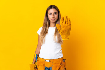 Young hispanic electrician woman over isolated yellow wall making stop gesture