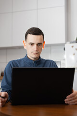 A young man working online with a laptop while sitting alone at a table inside his modern apartment