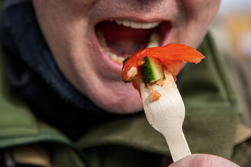 Man brings a fork with chopped vegetables to his mouth, close-up, focus on a fork with vegetables,...