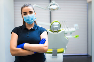 Fototapeta na wymiar Young female dentist doctor in mask stands in the office with his arms crossed