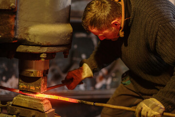 A blacksmith forging a red-hot iron billet on an automatic wall. Handicraft concept