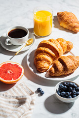 Breakfast concept. Fresh croissants with berries, cup of coffee and glass of orange juice on white marble background.