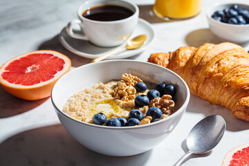 Breakfast concept. Oatmeal with berries and nuts, a cup of coffee and a glass of orange juice on a white marble background.