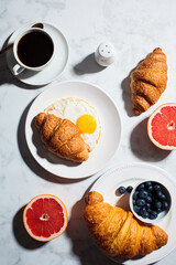 Breakfast flat lay. Fried egg with croissant, fruits, berries and cup of coffee on white marble background.