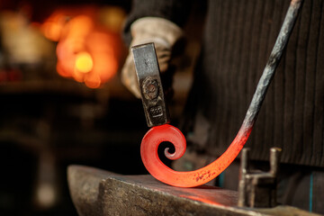 Close-up of the hands of a blacksmith twisting a spiral with a hammer, putting a red-hot iron blank...