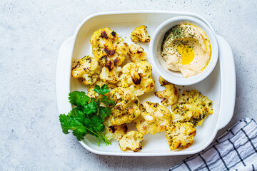 Baked cauliflower in white dish with hummus. Healthy food concept.