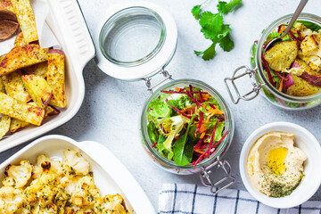 Cooking healthy food concept. Baked cauliflower, sweet potato, hummus and salad in jars on gray background, top view. Cooking food for the week.