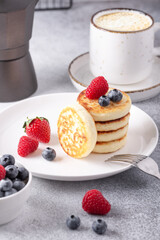 Cottage cheese pancakes with fresh berries, cup of coffee and coffee maker on stone table. Tasty breakfast food. Vertical photo - Image