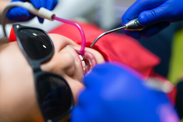 Dentist and assistant make preventive dental plaque cleaning for teenager