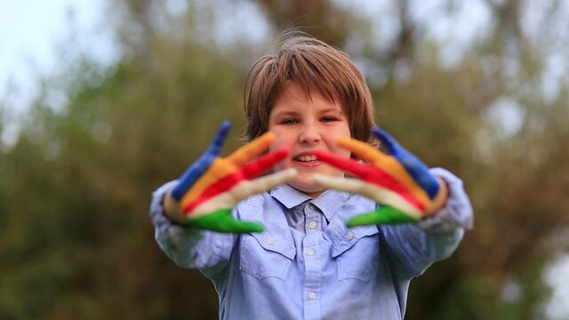 Kid play paint hands. Outdoor portrait of cheerful kid girl show hello gesture with hands painted in Seychelles flag colors.