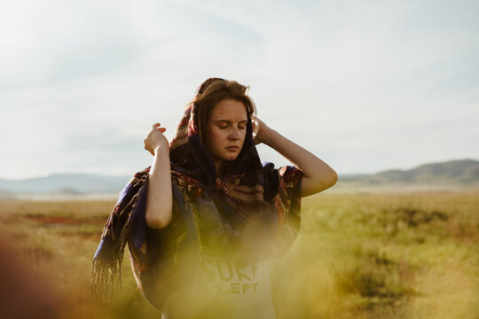 In the steppe raising her hands to the ears a girl with natural beauty in an ethno cape listens to the sound of the wind against the backdrop of the hills. High quality photo