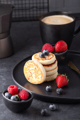 Close up of cheese pancakes with fresh berries on dark ceramic plate. Syrniki. Vertical photo - Image