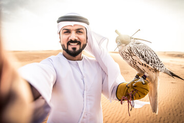 Arabic man with traditional emirates clothes walking in the desert with his falcon bird