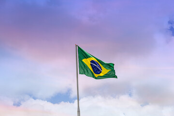 Bandeira do Brasil hasteada, balançando ao vento com o céu e nuvens ao fundo.