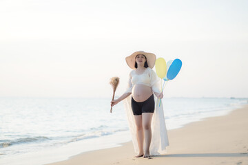 Asian pregnant woman holding balloons at beach .