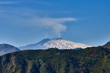 Obraz premium paragliding over the Etna volcano on a beautiful sunny day while the mountain smokes