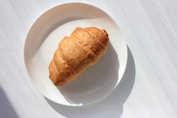 Croissant on plate on white background with copy space. French breakfast. Flat lay food. Sunny day. Direct light