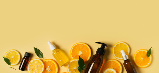 Bottles of serum of vitamin c and orange, lemon and green leaf flat lay on yellow background