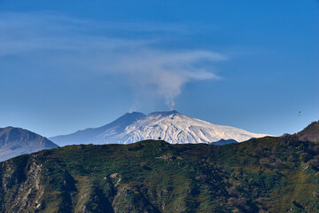 Fototapeta na wymiar paragliding over the Etna volcano on a beautiful sunny day while the mountain smokes