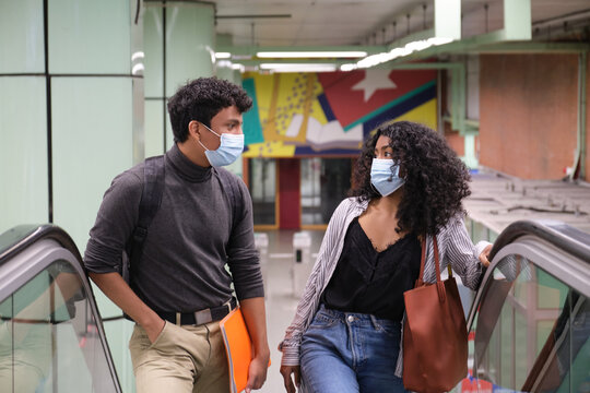 Young latin couple wearing protective face mask walking up into the escalators at the train or metro station. New normal at public transport.
