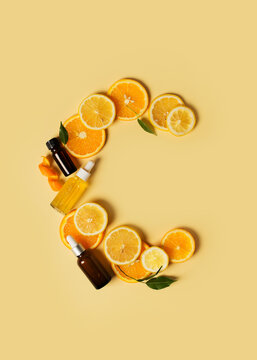 Bottles of serum of vitamin c and orange, lemon and green leaf flat lay on yellow background