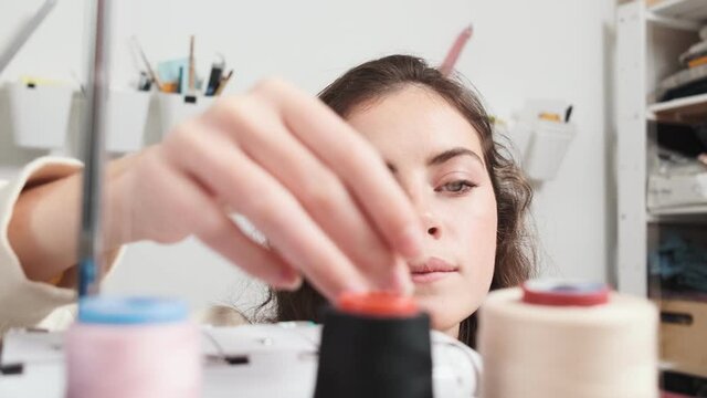 A close-up view of a focused young woman seamstress is working with a sewing machine at the design studio