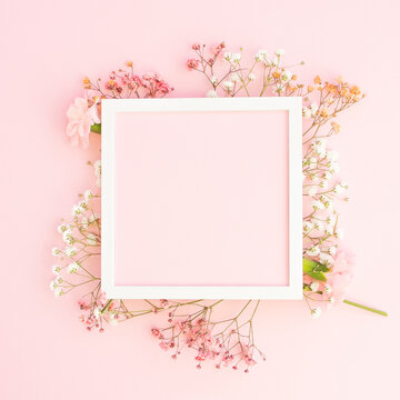 Creative spring greeting card design. Branches of white, and pink  gypsophila and fresh carnations  flowers with  square photo frame on pastel pink background. Birthday,  Mother's Day. Copy space.