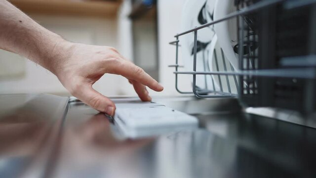 Man putting detergent tablet into dishwasher.