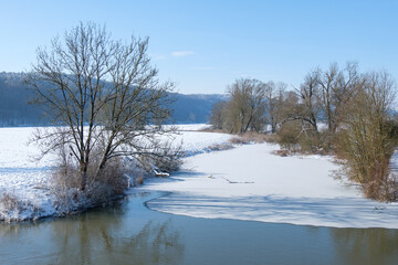 Naklejka na ściany i meble Winterliche Landschaft mit einem zugefrorenen Gewässer bei blauem Himmel und Schnee - rechts und links Ufer