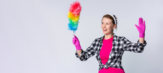 Banner- long format on gray background. Surprised young woman in pink gloves holding dust brush with hands up, looking side with shocked emotion on empty space for your advertisement