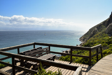 Fototapeta na wymiar Lookout point with wooden benches overlooking the sea and the mountains in Robberg Nature Reserve, Plettenberg Bay, South Africa.