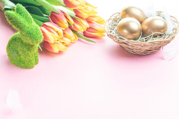 Easter egg. Happy Easter decoration: Golden eggs in basket with spring tulips, white feathers on pastel pink background. Traditional decoration in sun light.