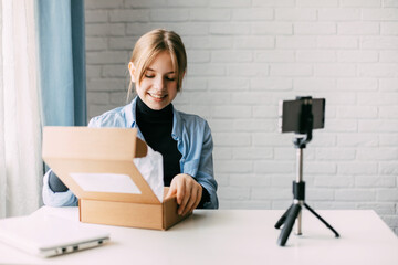 A teen blogger records a video and unpacks a box for his blog on a smartphone on a tripod at home....
