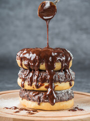 Chocolate donuts lying on top of each other, drizzled with chocolate on a wooden board. Dark background