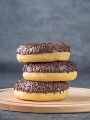 Chocolate donuts lying on top of each other on a wooden board. Dark background