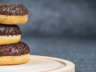 Chocolate donuts lying on top of each other on a wooden board. Dark background