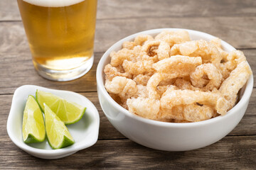Fried pork cracklings on a white bowl with lemon and beer over wooden table