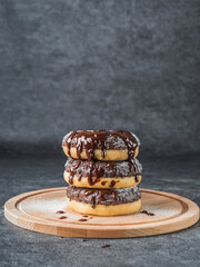 Chocolate donuts lying on top of each other, drizzled with chocolate on a wooden board. Dark background