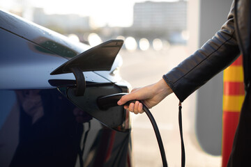 Cropped view of female hand, holding power cable supply plugged in electric car, charging...