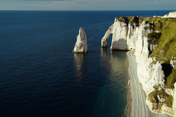 A rocky chalk cliffs with the Needle of Etretat near the emerald ocean. Spectacular view of the Etretra cliffs.         
