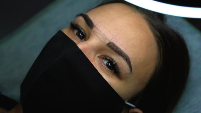 Beautiful young girl tweezing her brows in a beauty salon. Beauty Concept. Cosmetologist plucks client eyebrows by thread. Eyebrow correction, threading. Permanent Makeup. Microblading brow. Close up.